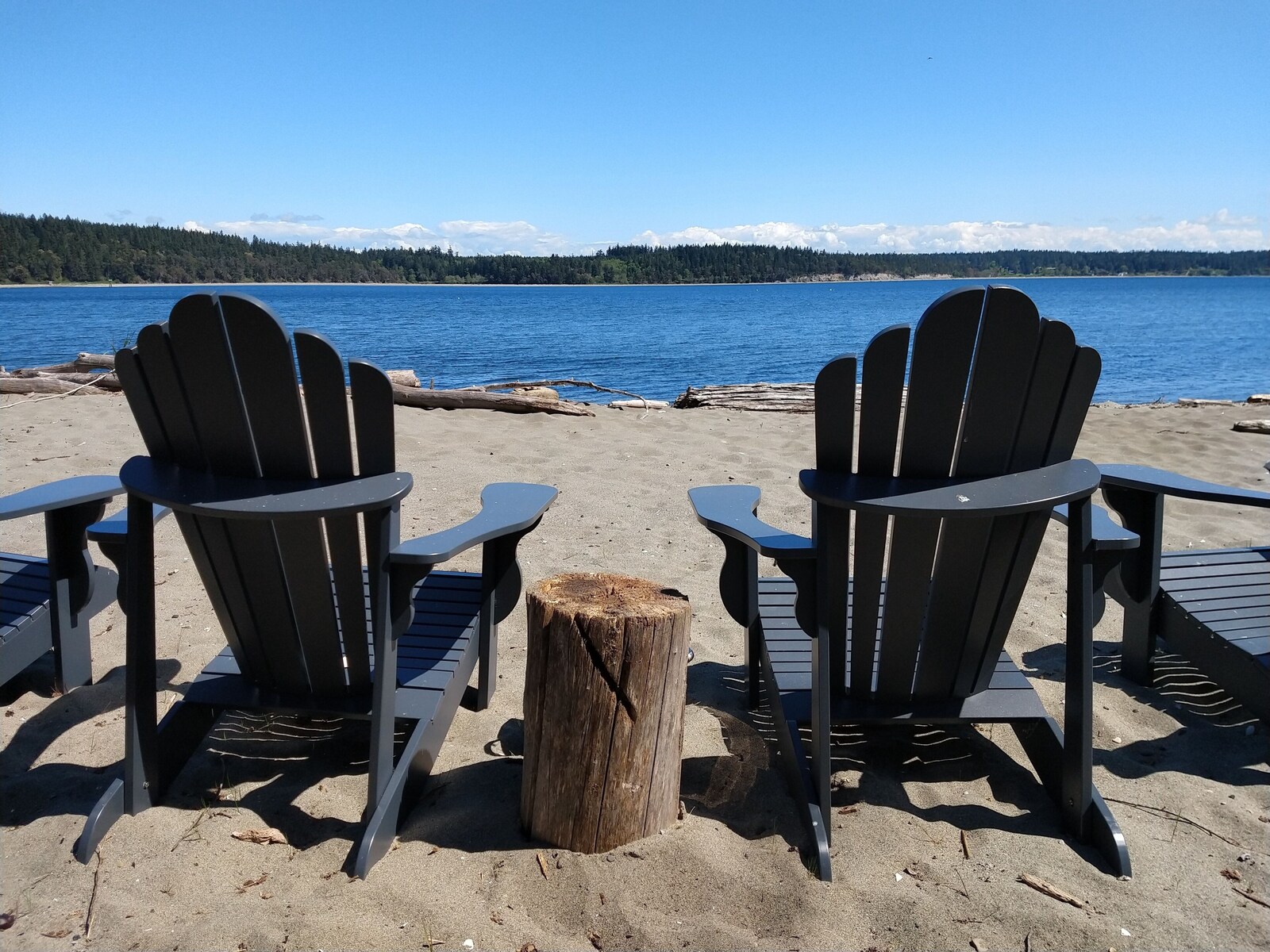 Adirondack chairs on the sandy beach facing the water